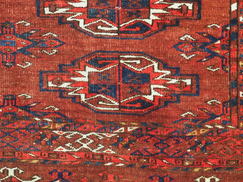 An antique rectangular Turkmen chuval wool textile featuring nine geometric gul motifs on a terracotta red ground with geometric borders. View IX