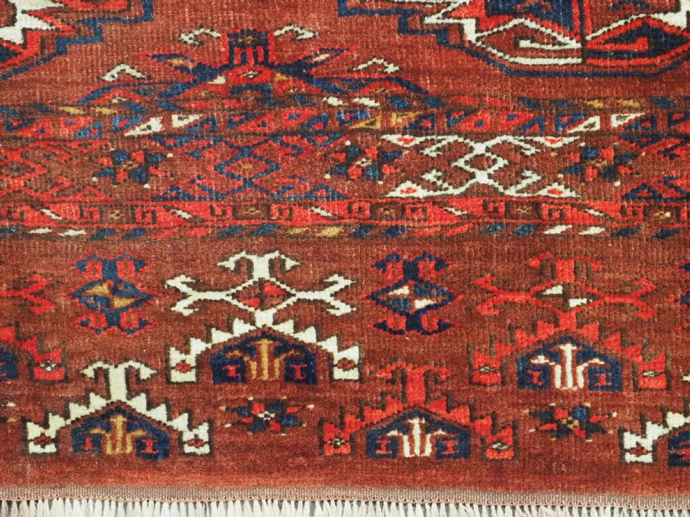 An antique rectangular Turkmen chuval wool textile featuring nine geometric gul motifs on a terracotta red ground with geometric borders. View X