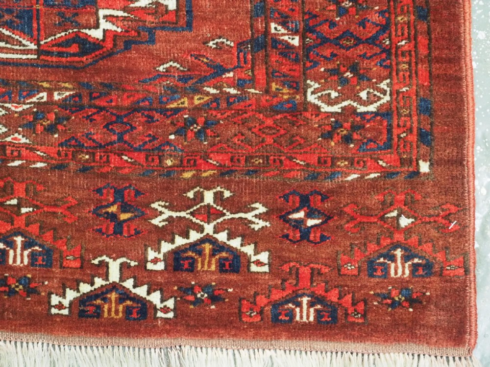 An antique rectangular Turkmen chuval wool textile featuring nine geometric gul motifs on a terracotta red ground with geometric borders. View XI