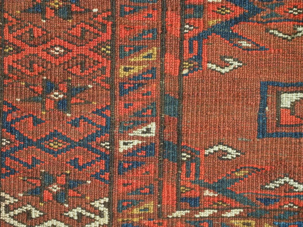 An antique rectangular Turkmen chuval wool textile featuring nine geometric gul motifs on a terracotta red ground with geometric borders. View XII