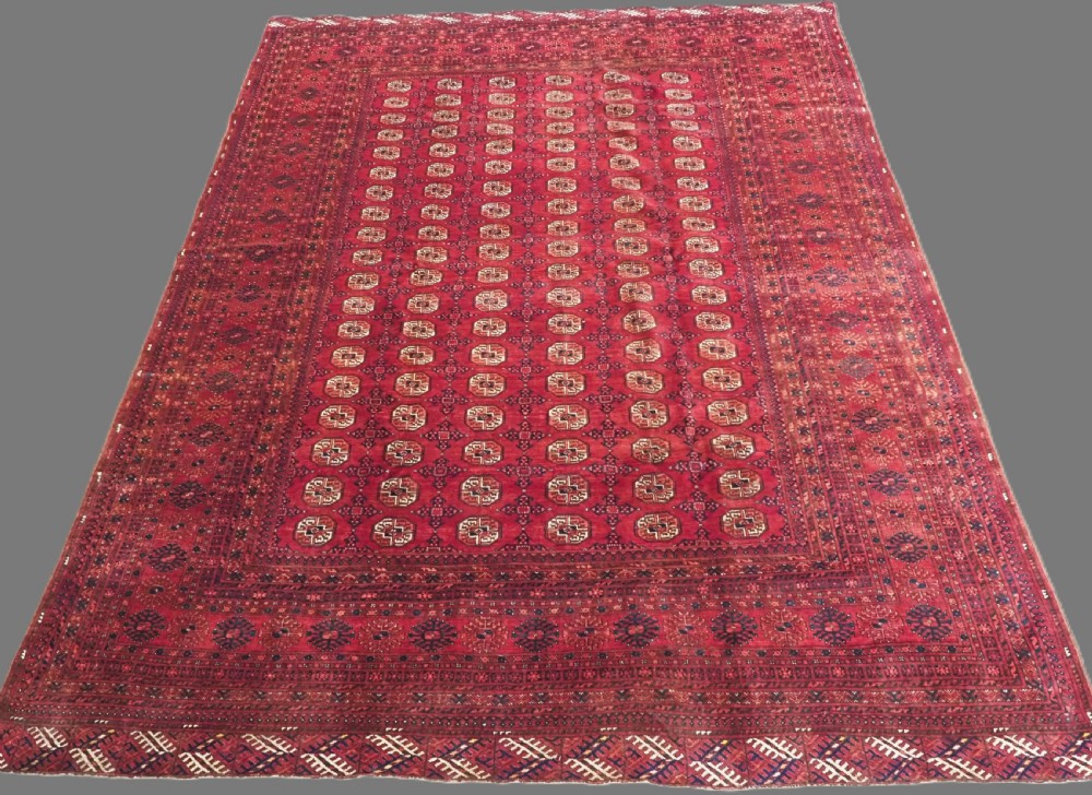 A large hand-knotted red wool carpet featuring repeated octagonal gul motifs across the central field with geometric borders.