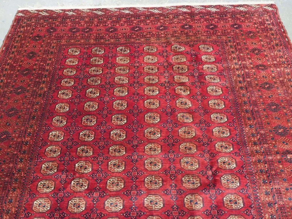 A large hand-knotted red wool carpet featuring repeated octagonal gul motifs across the central field with geometric borders. View III