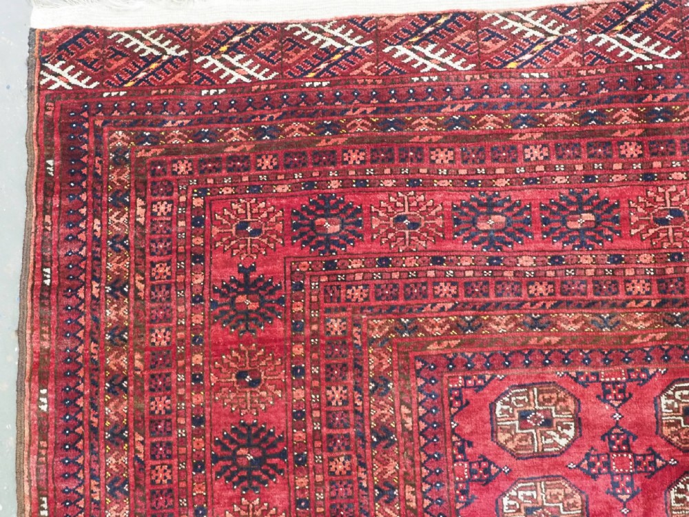 A large hand-knotted red wool carpet featuring repeated octagonal gul motifs across the central field with geometric borders. View V