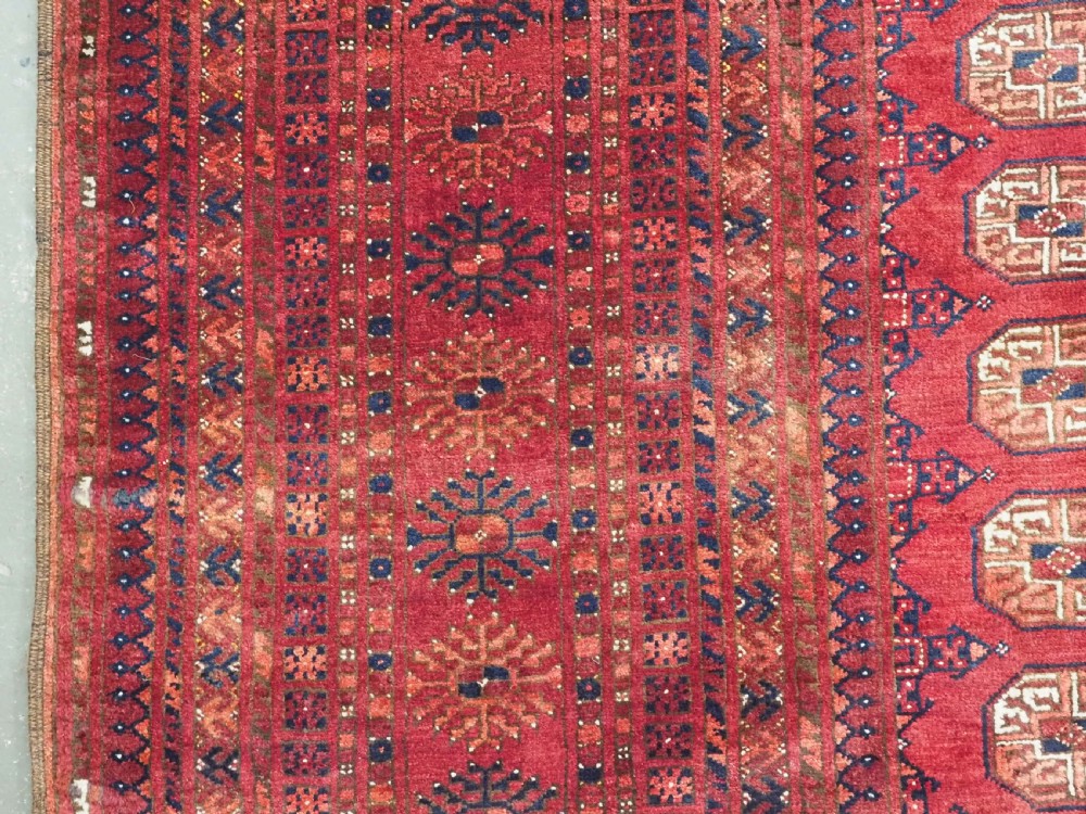 A large hand-knotted red wool carpet featuring repeated octagonal gul motifs across the central field with geometric borders. View VII