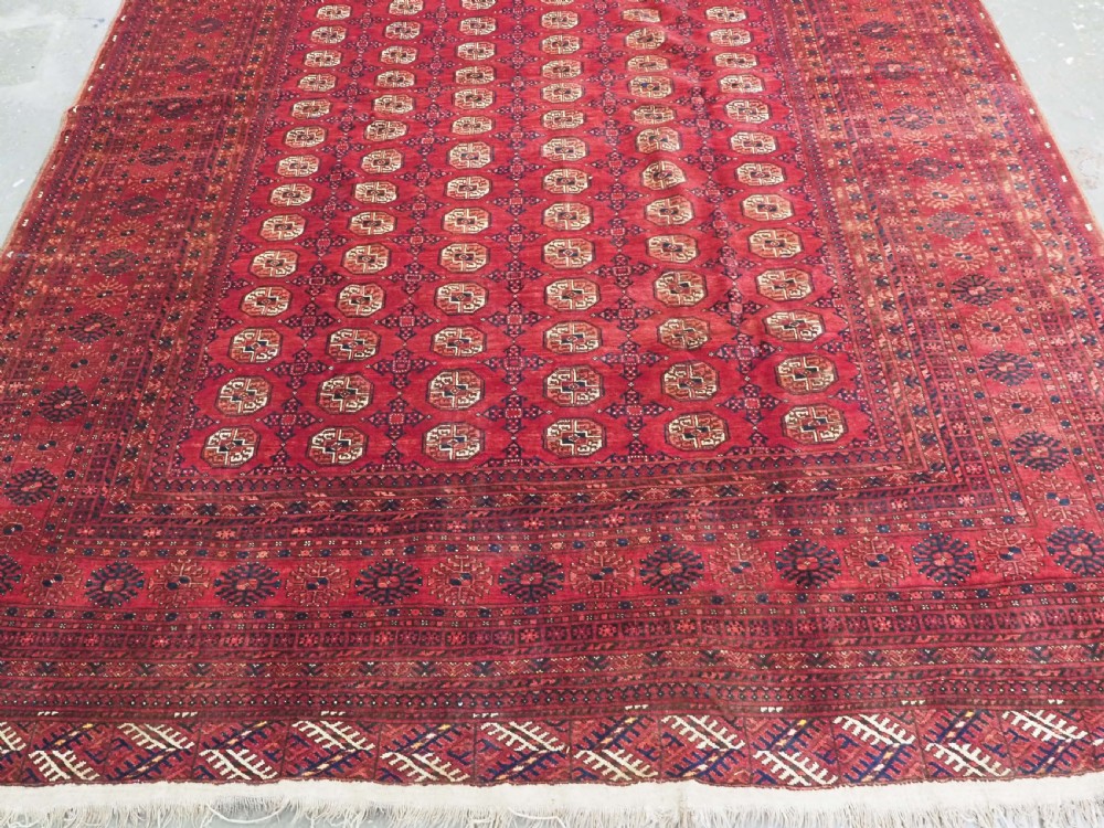 A large hand-knotted red wool carpet featuring repeated octagonal gul motifs across the central field with geometric borders. View XII