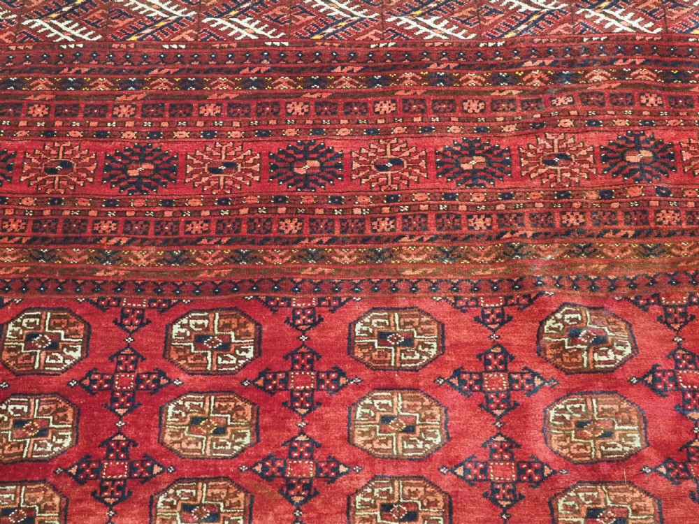 A large hand-knotted red wool carpet featuring repeated octagonal gul motifs across the central field with geometric borders. View XV