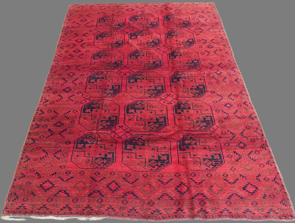 An antique rectangular wool carpet featuring a warm red field decorated with grid-arranged octagonal gul motifs within a geometric border.
