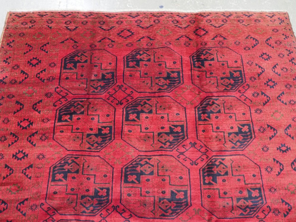 An antique rectangular wool carpet featuring a warm red field decorated with grid-arranged octagonal gul motifs within a geometric border. View III