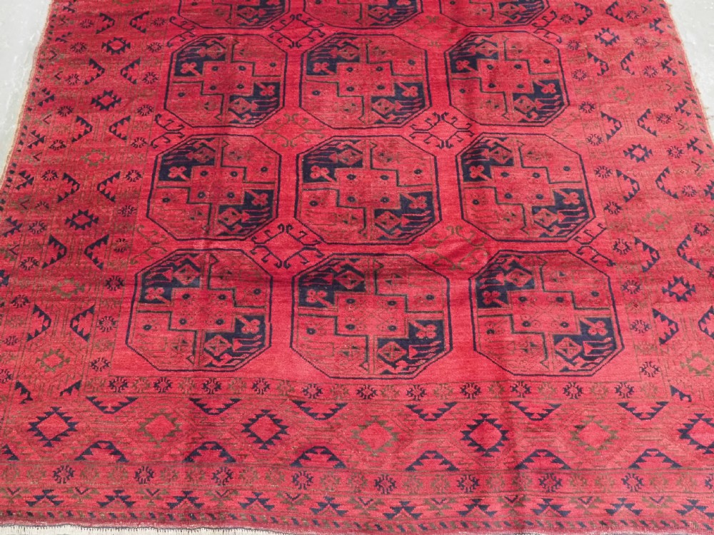An antique rectangular wool carpet featuring a warm red field decorated with grid-arranged octagonal gul motifs within a geometric border. View V