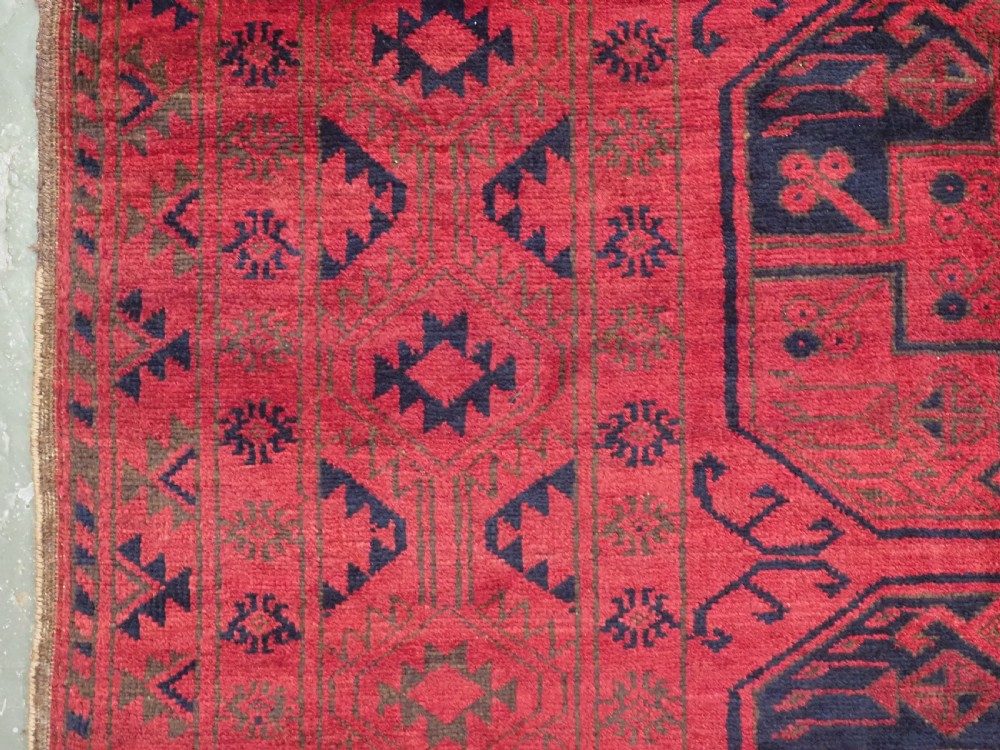 An antique rectangular wool carpet featuring a warm red field decorated with grid-arranged octagonal gul motifs within a geometric border. View VI