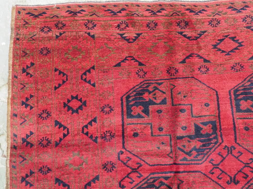 An antique rectangular wool carpet featuring a warm red field decorated with grid-arranged octagonal gul motifs within a geometric border. View VII