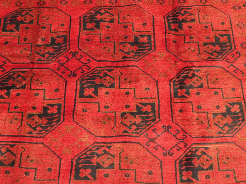 An antique rectangular wool carpet featuring a warm red field decorated with grid-arranged octagonal gul motifs within a geometric border. View VIII