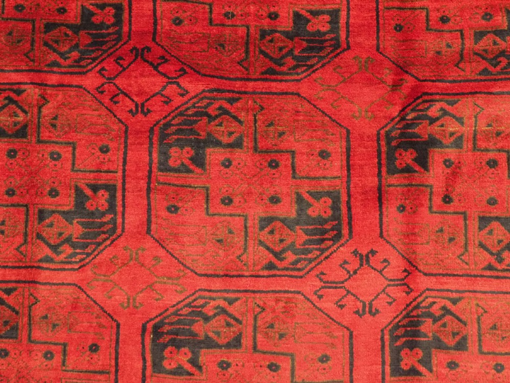 An antique rectangular wool carpet featuring a warm red field decorated with grid-arranged octagonal gul motifs within a geometric border. View IX
