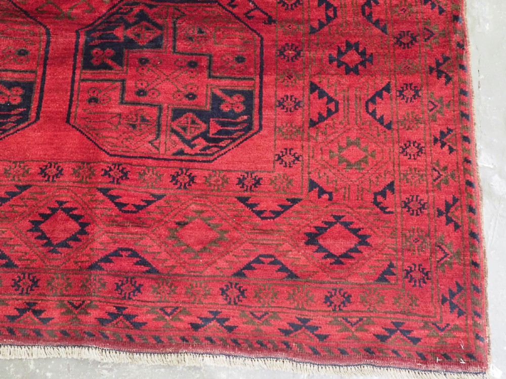 An antique rectangular wool carpet featuring a warm red field decorated with grid-arranged octagonal gul motifs within a geometric border. View XI