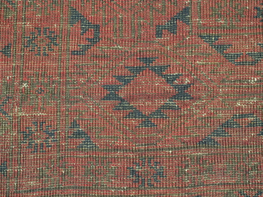 An antique rectangular wool carpet featuring a warm red field decorated with grid-arranged octagonal gul motifs within a geometric border. View XII