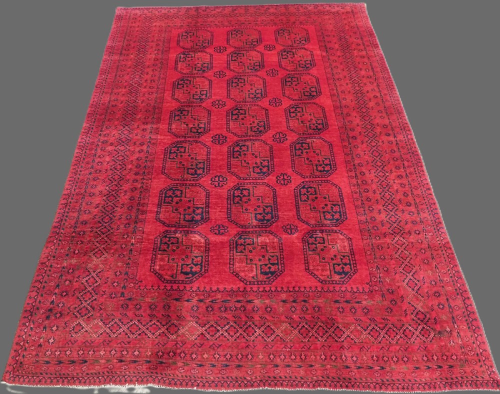 An antique hand-knotted wool carpet featuring repeating octagonal gul motifs on a deep crimson field surrounded by geometric patterned borders.