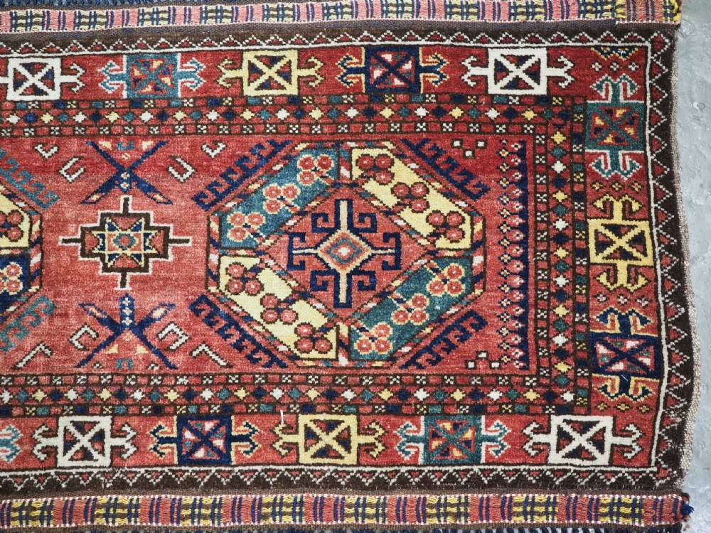A small rectangular Central Asian wool weaving featuring geometric Turkmen gol motifs in blue and yellow on a red ground with multi-coloured fringe borders. View IV