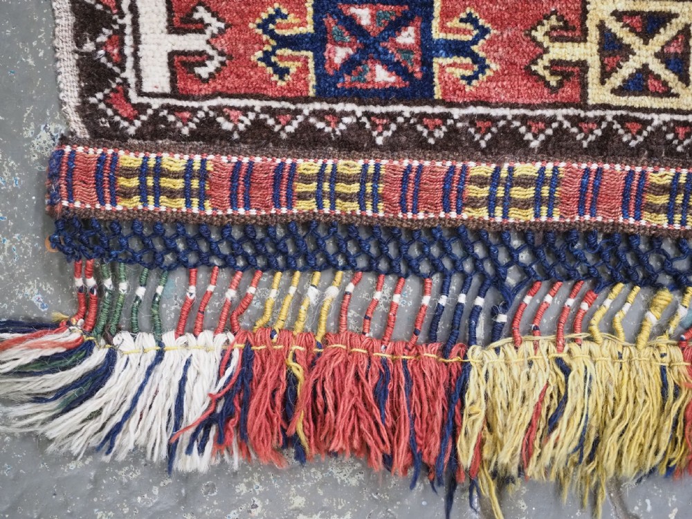 A small rectangular Central Asian wool weaving featuring geometric Turkmen gol motifs in blue and yellow on a red ground with multi-coloured fringe borders. View VIII