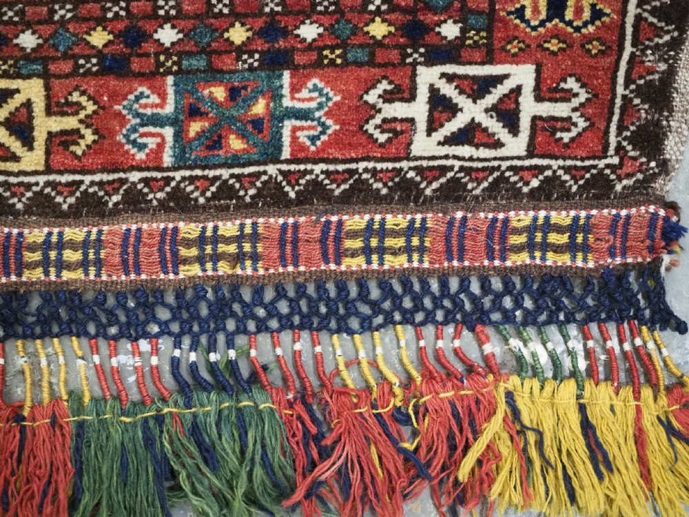 A small rectangular Central Asian wool weaving featuring geometric Turkmen gol motifs in blue and yellow on a red ground with multi-coloured fringe borders. View IX
