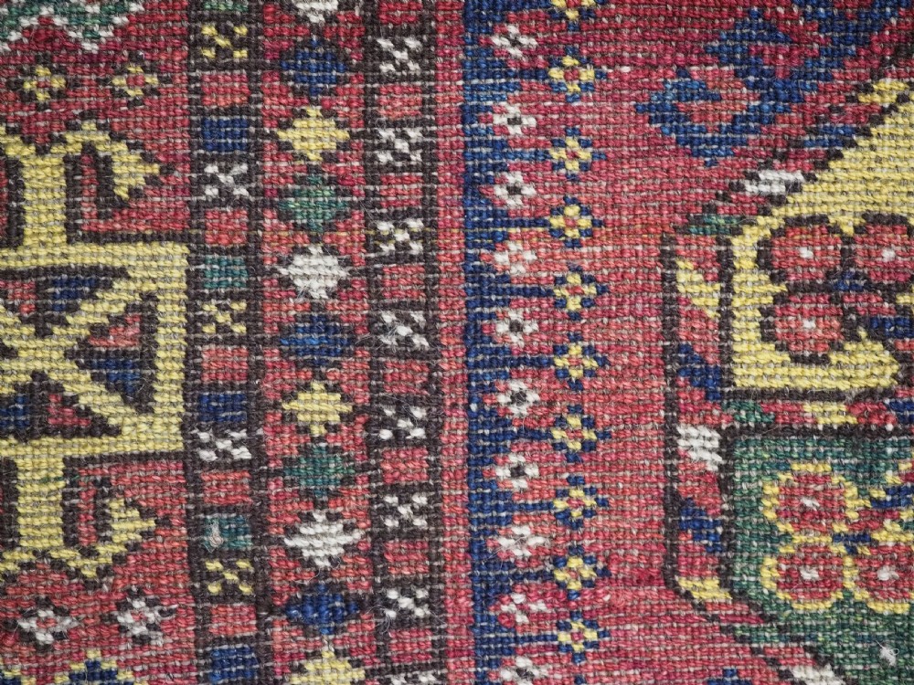 A small rectangular Central Asian wool weaving featuring geometric Turkmen gol motifs in blue and yellow on a red ground with multi-coloured fringe borders. View X