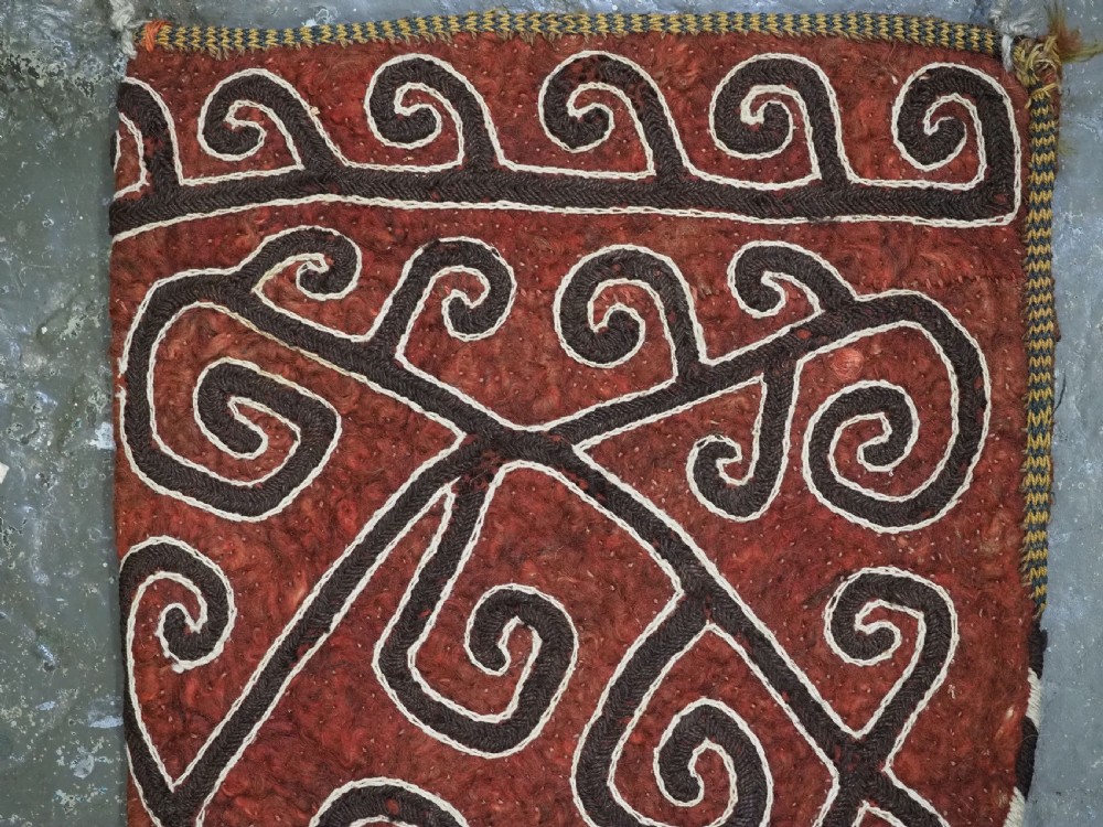 A terracotta red felt panel embroidered with off-white and dark brown scroll motifs, featuring cascading tier tassels made of dark horsehair. View II