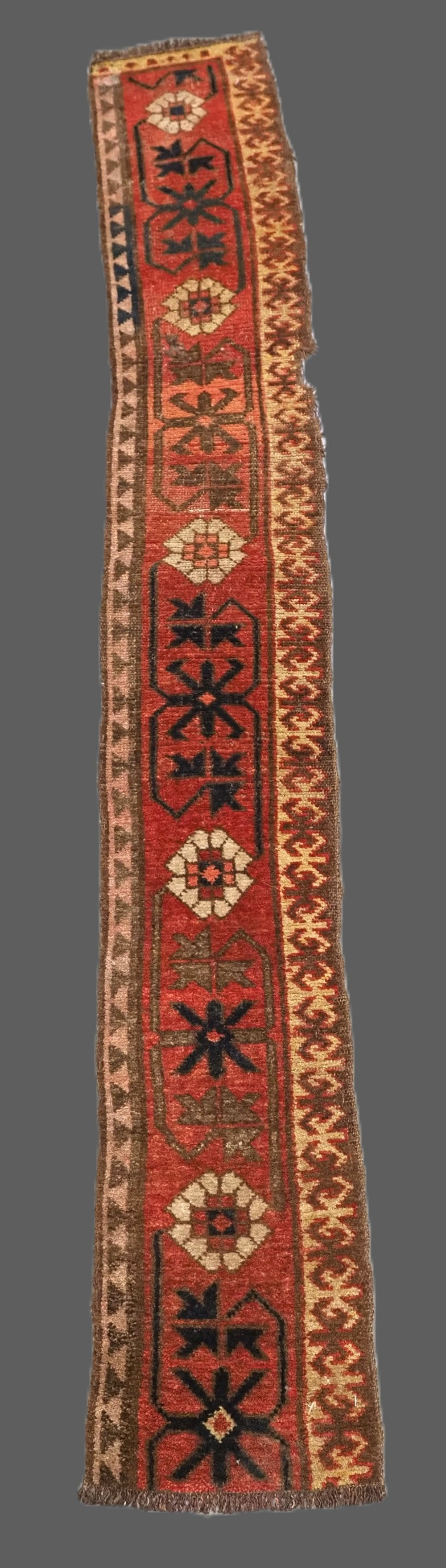 A long, narrow antique Kyrgyz woven wool tegerich fragment featuring geometric star motifs on a deep red background with brown decorative borders.
