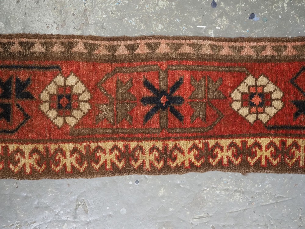 A long, narrow antique Kyrgyz woven wool tegerich fragment featuring geometric star motifs on a deep red background with brown decorative borders. View V