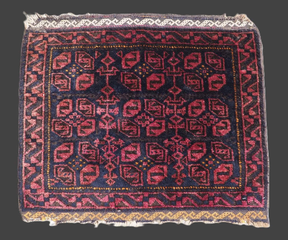 An antique hand-woven Baluch saddle bag face featuring dark red and navy geometric tile patterns with flatwoven web borders.
