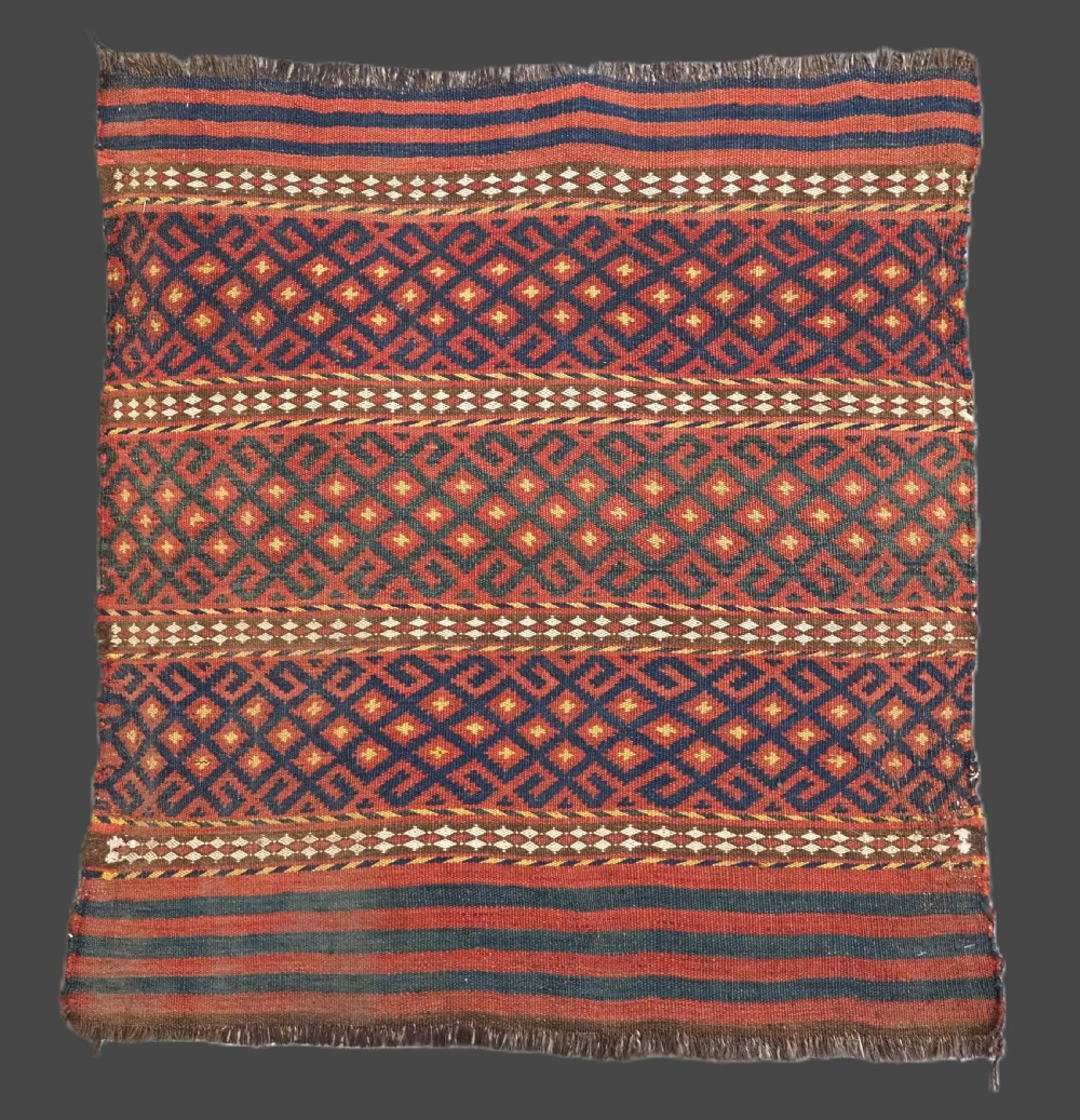A square handwoven wool Uzbek saddlebag face displaying red and navy blue geometric diamond lattice patterns between banded horizontal stripes.