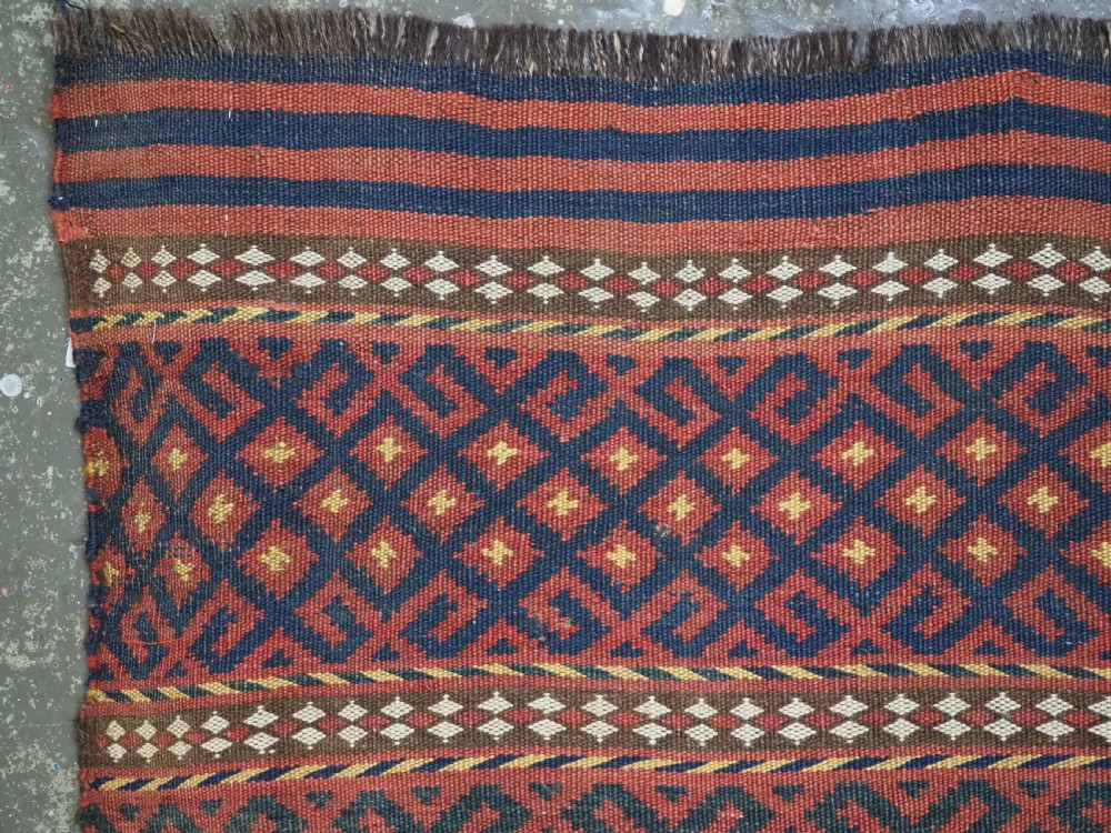 A square handwoven wool Uzbek saddlebag face displaying red and navy blue geometric diamond lattice patterns between banded horizontal stripes. View II
