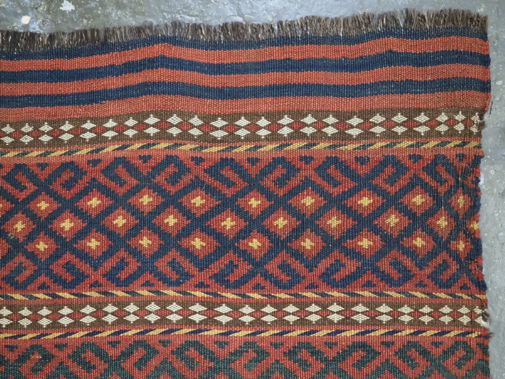 A square handwoven wool Uzbek saddlebag face displaying red and navy blue geometric diamond lattice patterns between banded horizontal stripes. View III