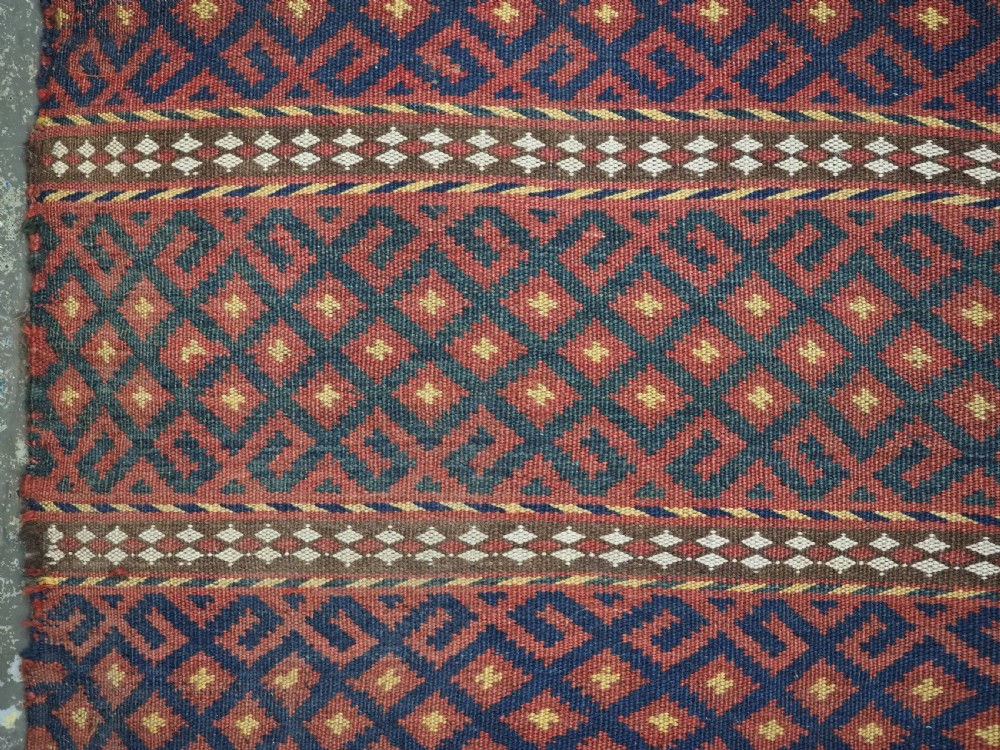 A square handwoven wool Uzbek saddlebag face displaying red and navy blue geometric diamond lattice patterns between banded horizontal stripes. View IV