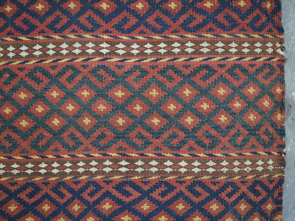 A square handwoven wool Uzbek saddlebag face displaying red and navy blue geometric diamond lattice patterns between banded horizontal stripes. View V