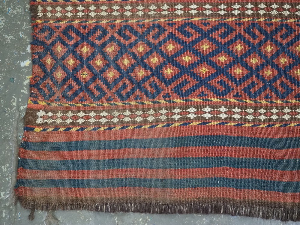 A square handwoven wool Uzbek saddlebag face displaying red and navy blue geometric diamond lattice patterns between banded horizontal stripes. View VI
