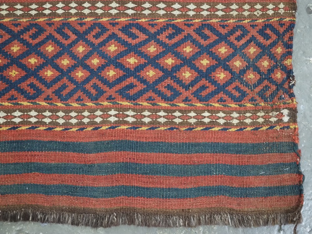 A square handwoven wool Uzbek saddlebag face displaying red and navy blue geometric diamond lattice patterns between banded horizontal stripes. View VII
