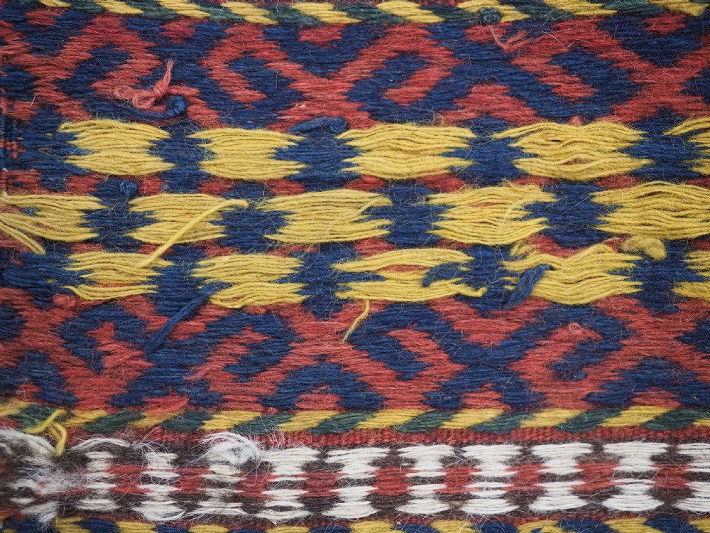 A square handwoven wool Uzbek saddlebag face displaying red and navy blue geometric diamond lattice patterns between banded horizontal stripes. View IX