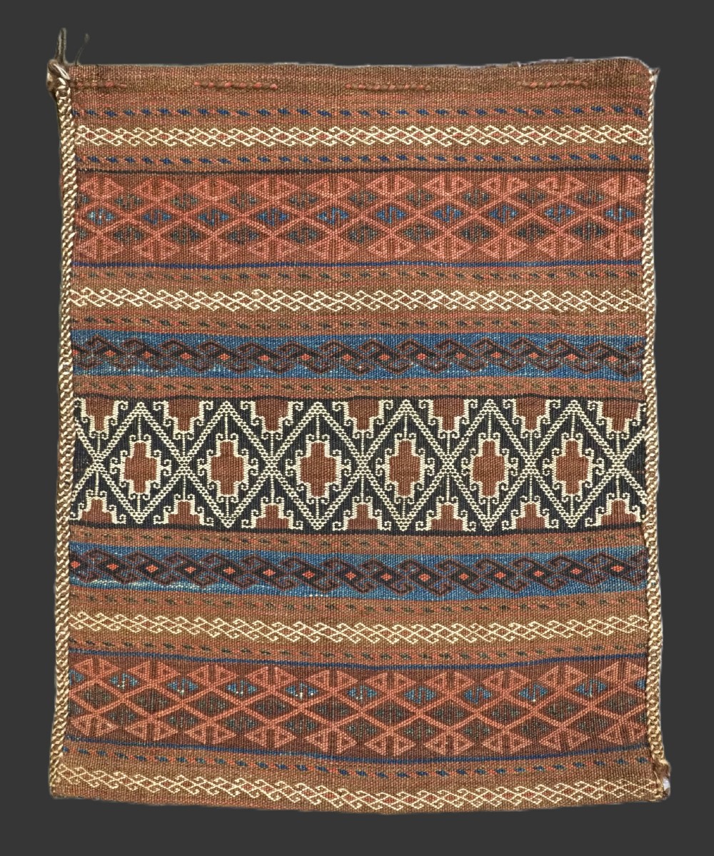 An antique woven Baluch storage bag featuring horizontal bands of geometric diamond motifs in terracotta, indigo blue, and cream wool.