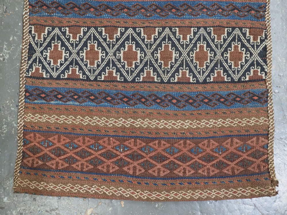 An antique woven Baluch storage bag featuring horizontal bands of geometric diamond motifs in terracotta, indigo blue, and cream wool. View III