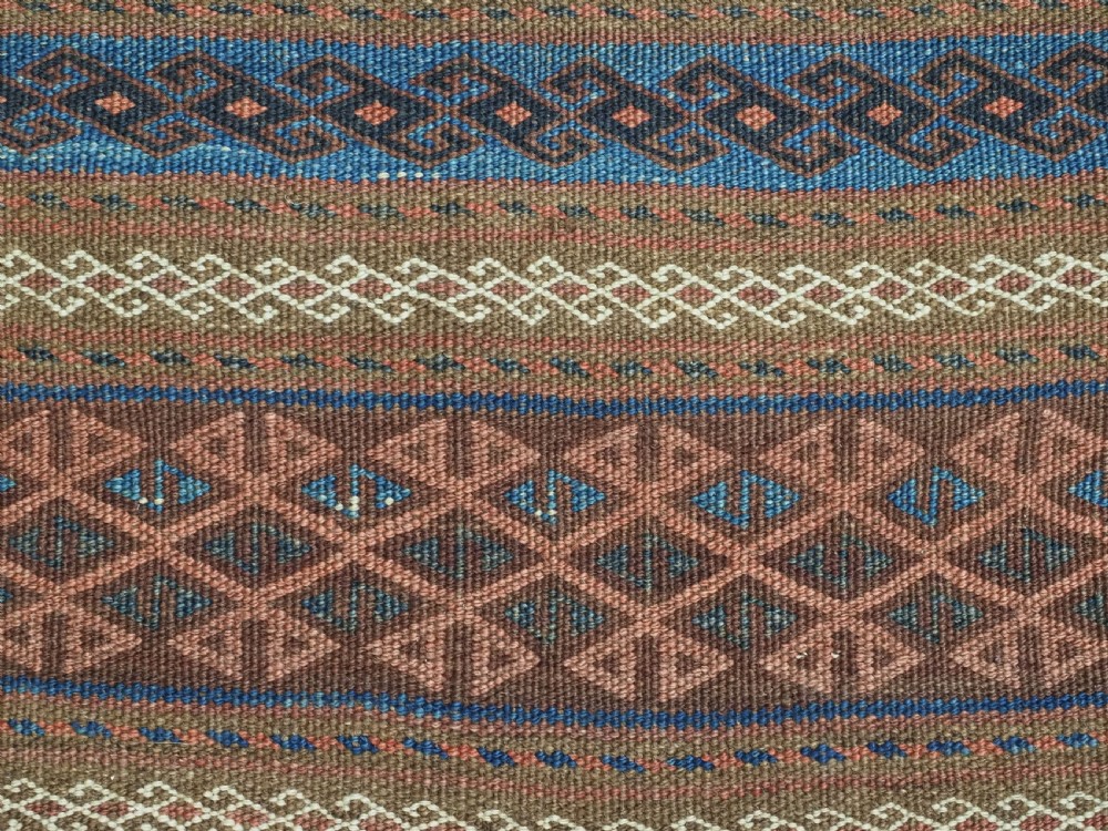 An antique woven Baluch storage bag featuring horizontal bands of geometric diamond motifs in terracotta, indigo blue, and cream wool. View V