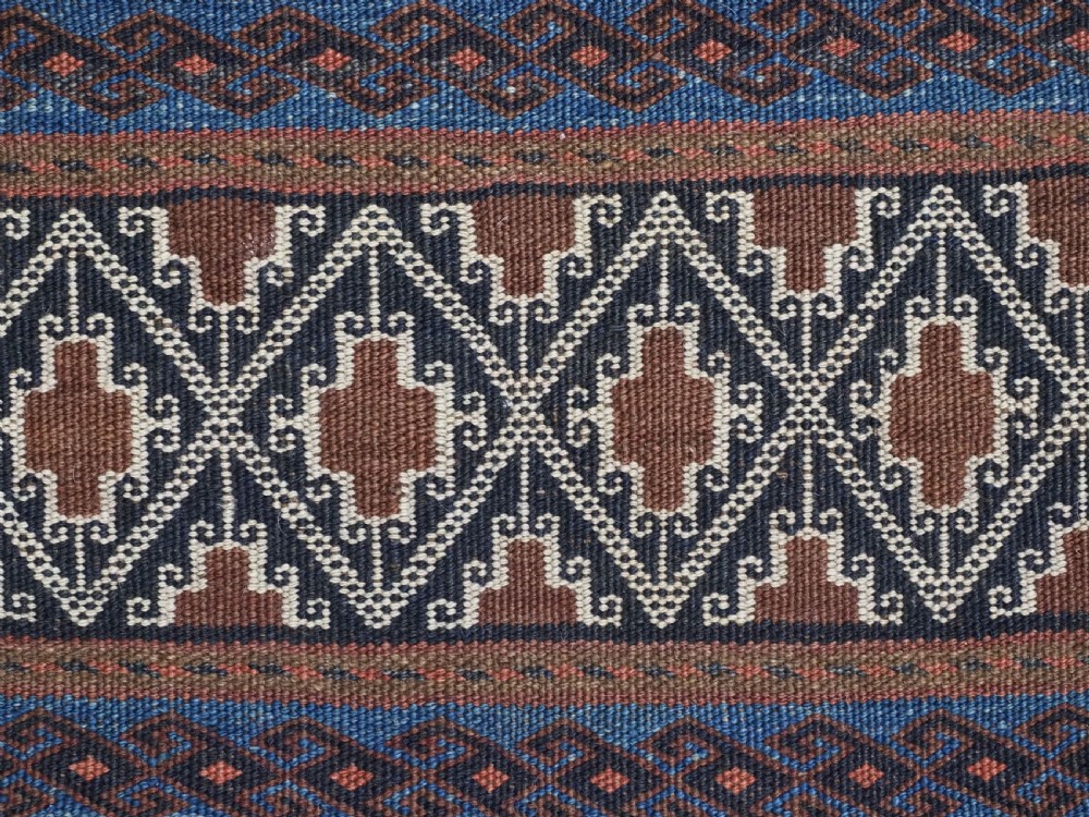 An antique woven Baluch storage bag featuring horizontal bands of geometric diamond motifs in terracotta, indigo blue, and cream wool. View VI