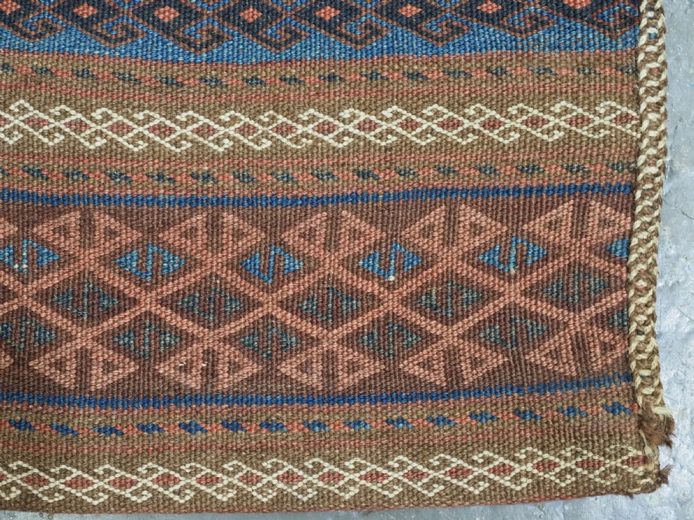 An antique woven Baluch storage bag featuring horizontal bands of geometric diamond motifs in terracotta, indigo blue, and cream wool. View VII