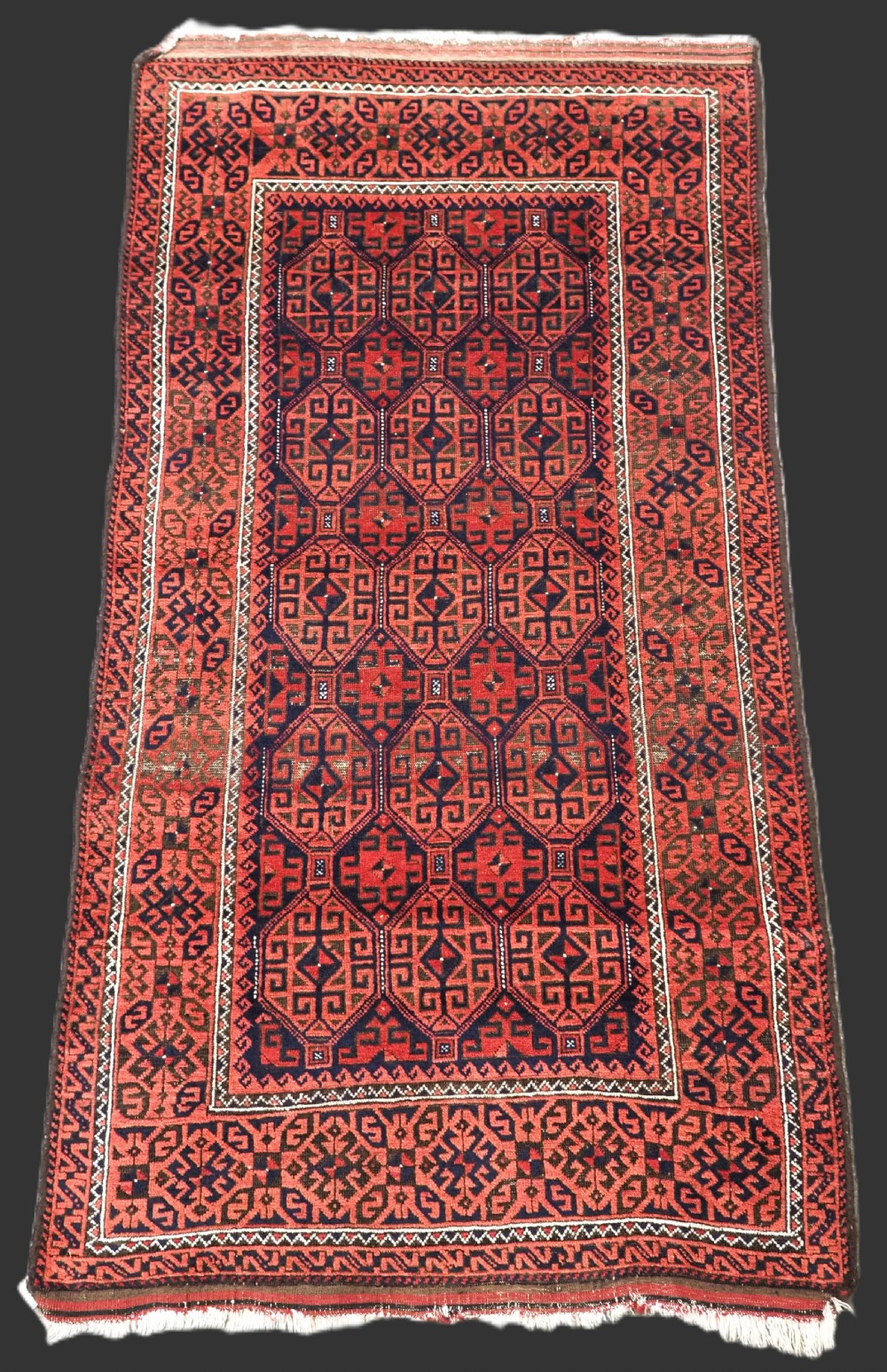 An antique hand-knotted wool rug featuring repeating geometric octagonal motifs in terracotta red and dark indigo blue.