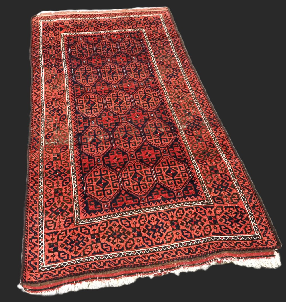 An antique hand-knotted wool rug featuring repeating geometric octagonal motifs in terracotta red and dark indigo blue. View II