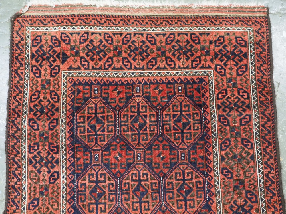 An antique hand-knotted wool rug featuring repeating geometric octagonal motifs in terracotta red and dark indigo blue. View III