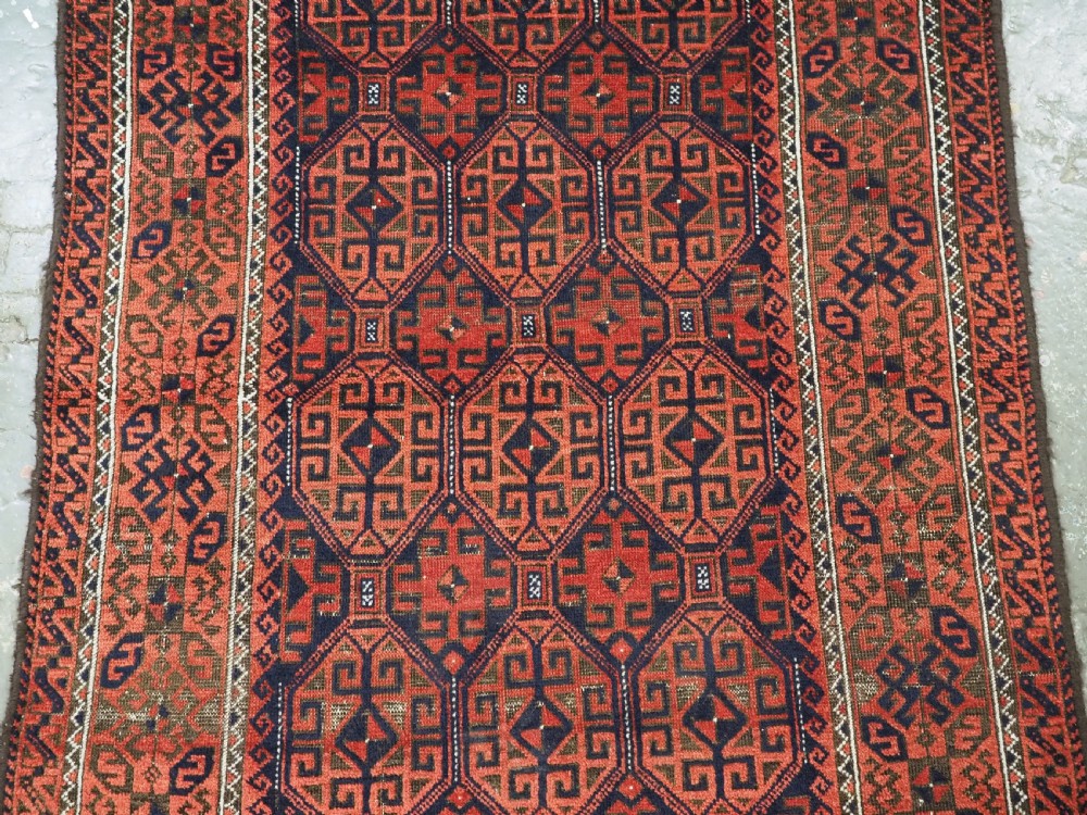 An antique hand-knotted wool rug featuring repeating geometric octagonal motifs in terracotta red and dark indigo blue. View IV