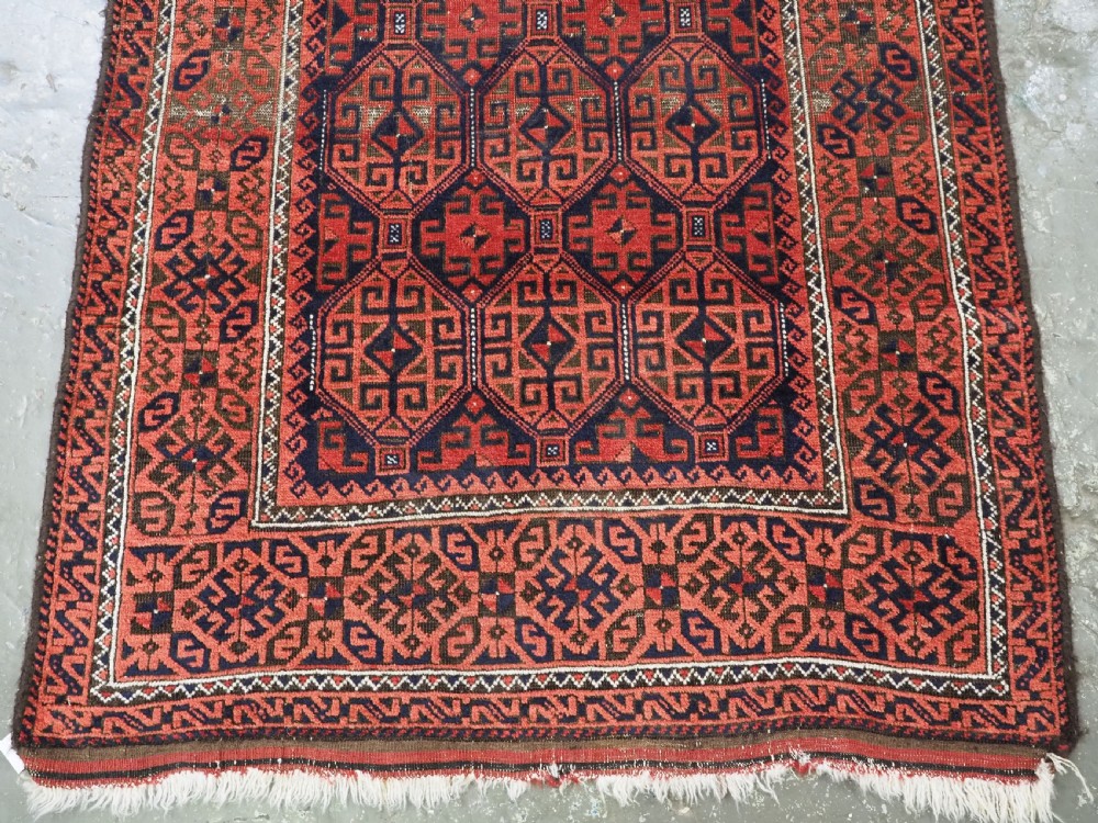 An antique hand-knotted wool rug featuring repeating geometric octagonal motifs in terracotta red and dark indigo blue. View V