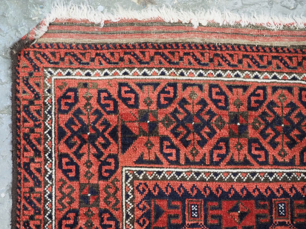 An antique hand-knotted wool rug featuring repeating geometric octagonal motifs in terracotta red and dark indigo blue. View VI