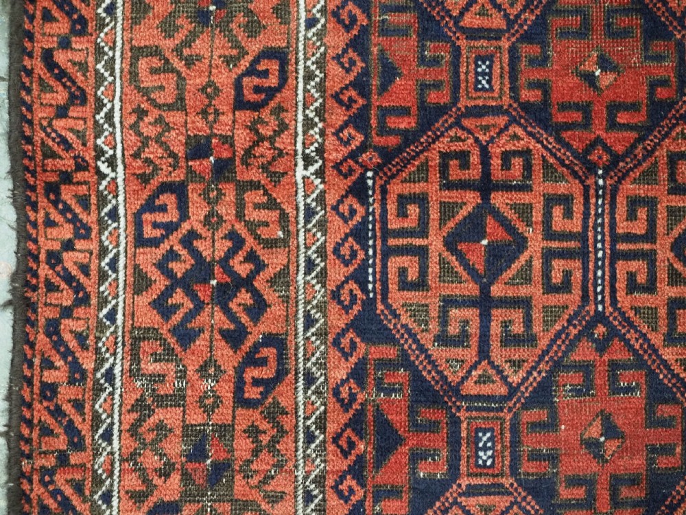 An antique hand-knotted wool rug featuring repeating geometric octagonal motifs in terracotta red and dark indigo blue. View VII