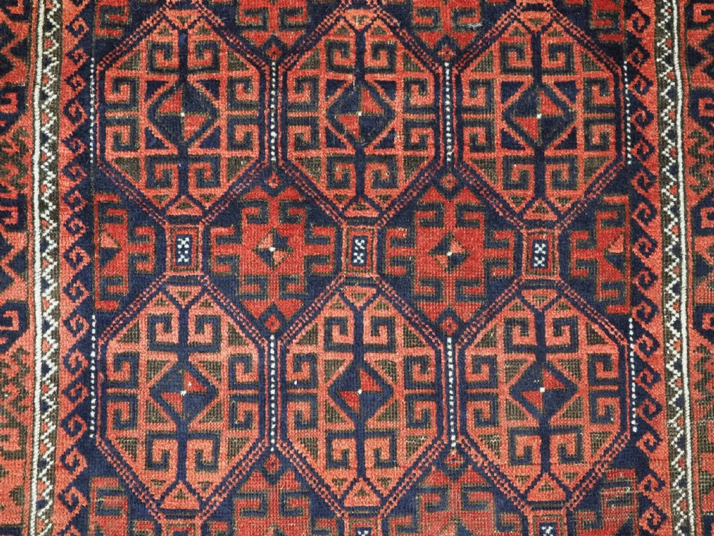 An antique hand-knotted wool rug featuring repeating geometric octagonal motifs in terracotta red and dark indigo blue. View IX