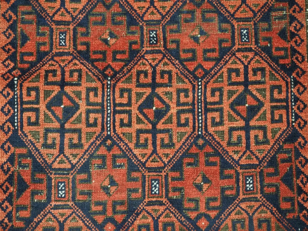 An antique hand-knotted wool rug featuring repeating geometric octagonal motifs in terracotta red and dark indigo blue. View X